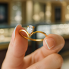 Gold ring with a diamond held by a hand against a blurred background