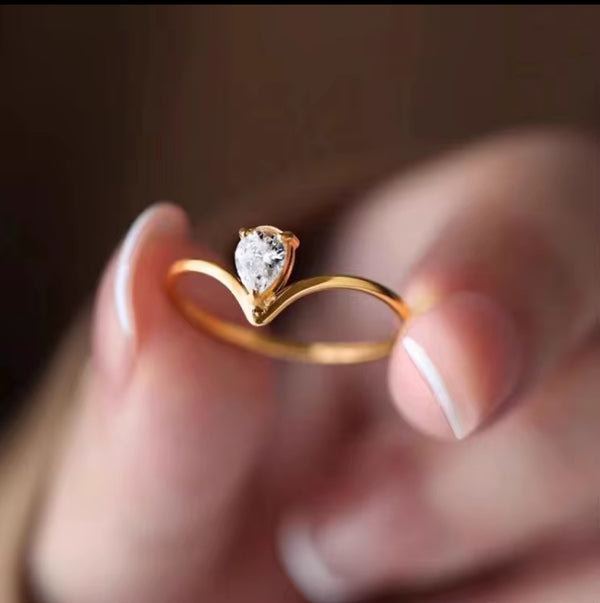 Gold ring with a heart-shaped diamond held between fingers against a blurred background