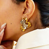 Gold butterfly earrings worn by a person with a neutral background